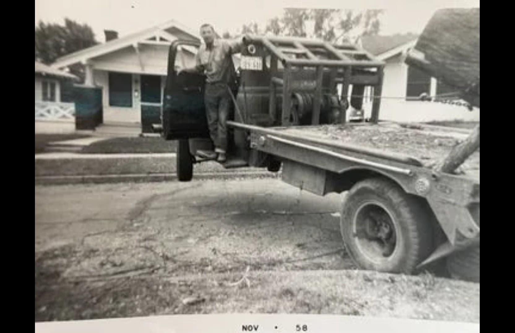 Man standing on a vintage truck with front wheels lifted high off the ground.
