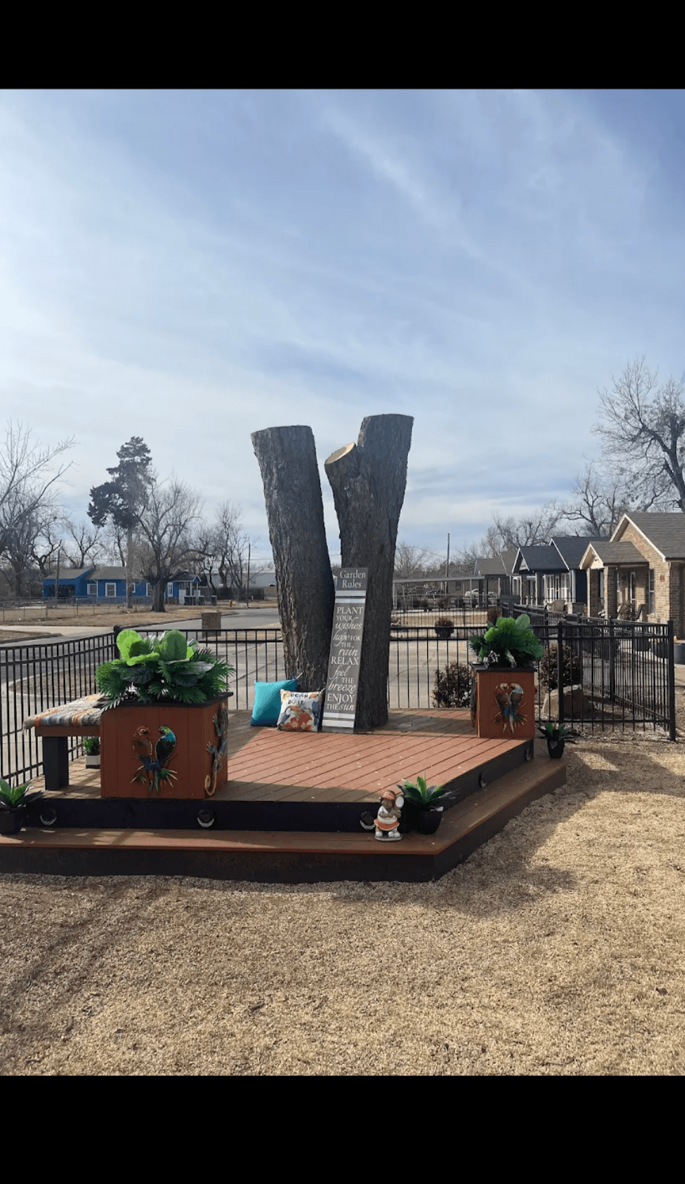 Large V-shaped tree stump on a wooden deck with planters, pillows, and garden decorations.